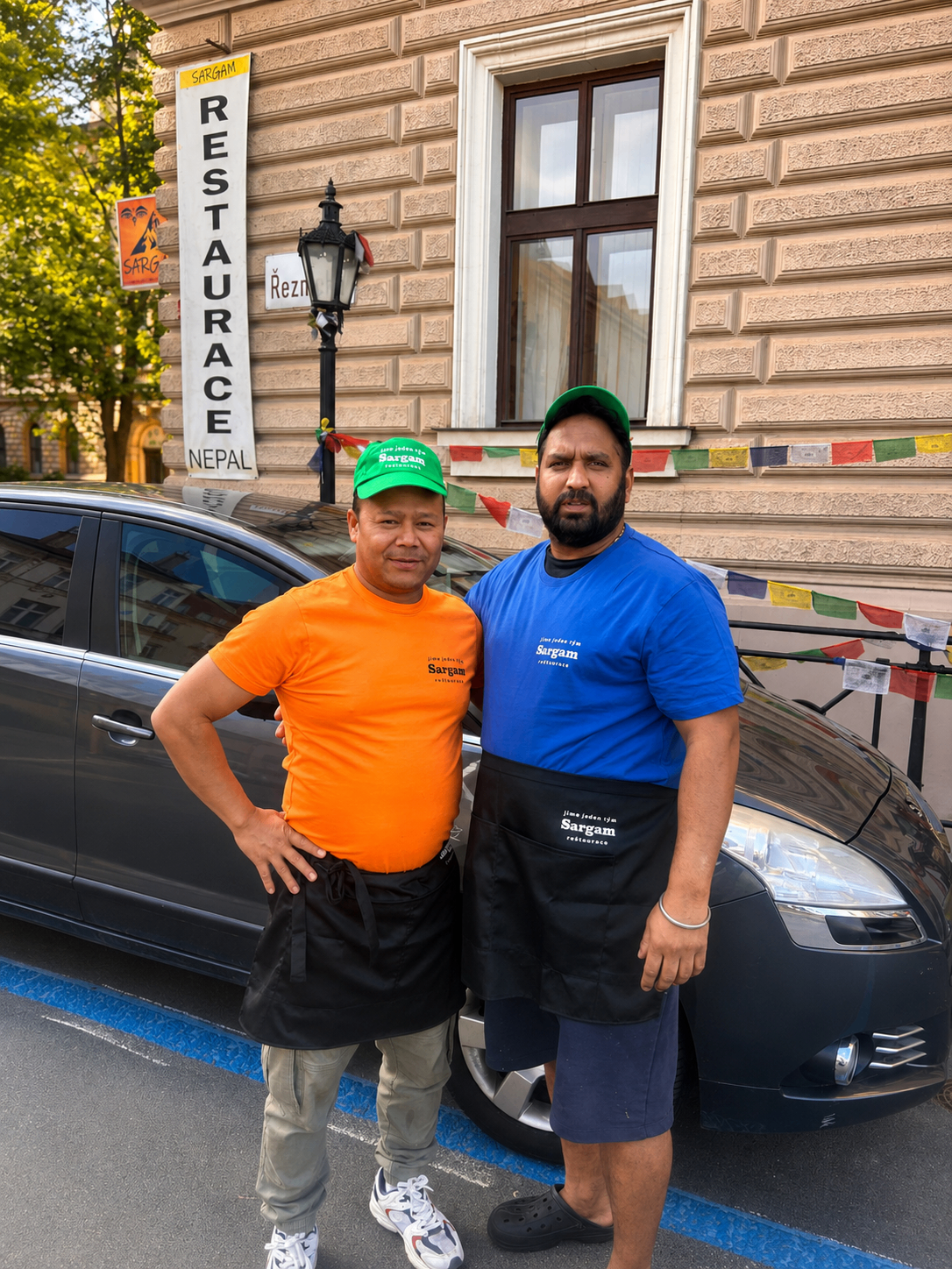 Dva členové týmu Sargam 1 před restaurací a zaparkovaným autem