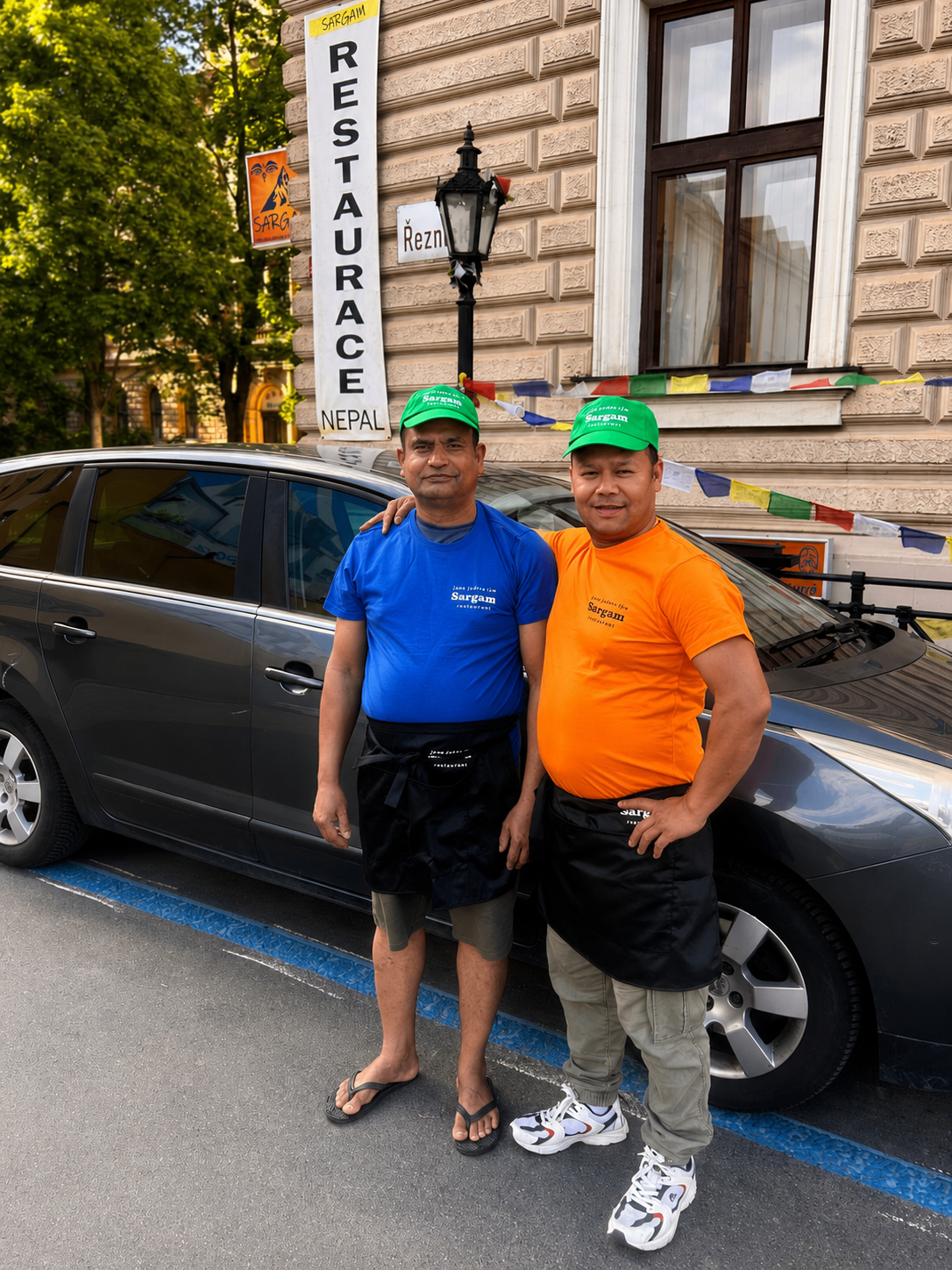 Dva členové týmu Sargam 1 v modrém a oranžovém tričku před restaurací